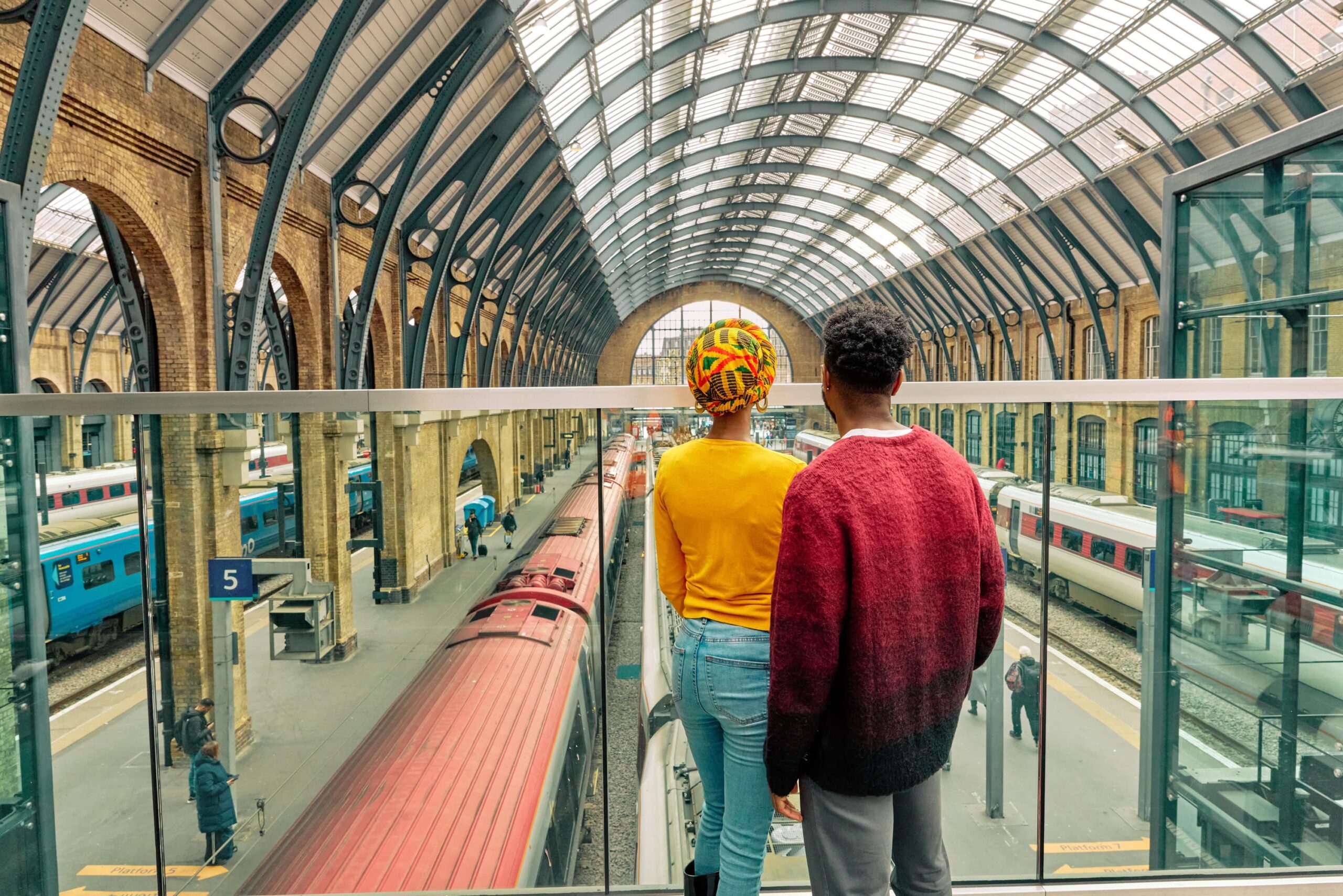 A couple stand on a raised walkway above station platforms, looking at the trains.